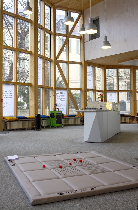 The Big Conversation Space (Niki Korth et Clémence de Montgolfier), Hearing all sides of the story, Paris Art Lab (cur. Leslie Veisse), Paris, 2020. Vue d'installation : série de huit drapeaux, impressions numériques sur tissu ; station d'enregistrement audio, techniques mixtes ; Conversation mat, matelas, impressions en sérigraphie, pierres, laine, livrets de traduction.