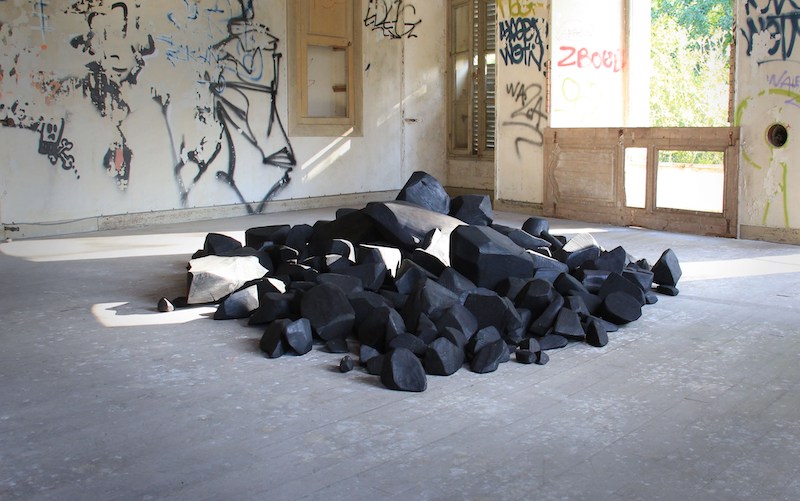 Lélia Demoisy, Fossilisation forcée, 2020 Bois de cèdre bleu Transformation d'un tronc de cèdre bleu de 3 m de long et de 70 cm de diamètre en un tas de pierre s'étalant sur une surface de 8 m². Un micro paysage minéral, carbonisé, qui a pourtant bien été vivant.